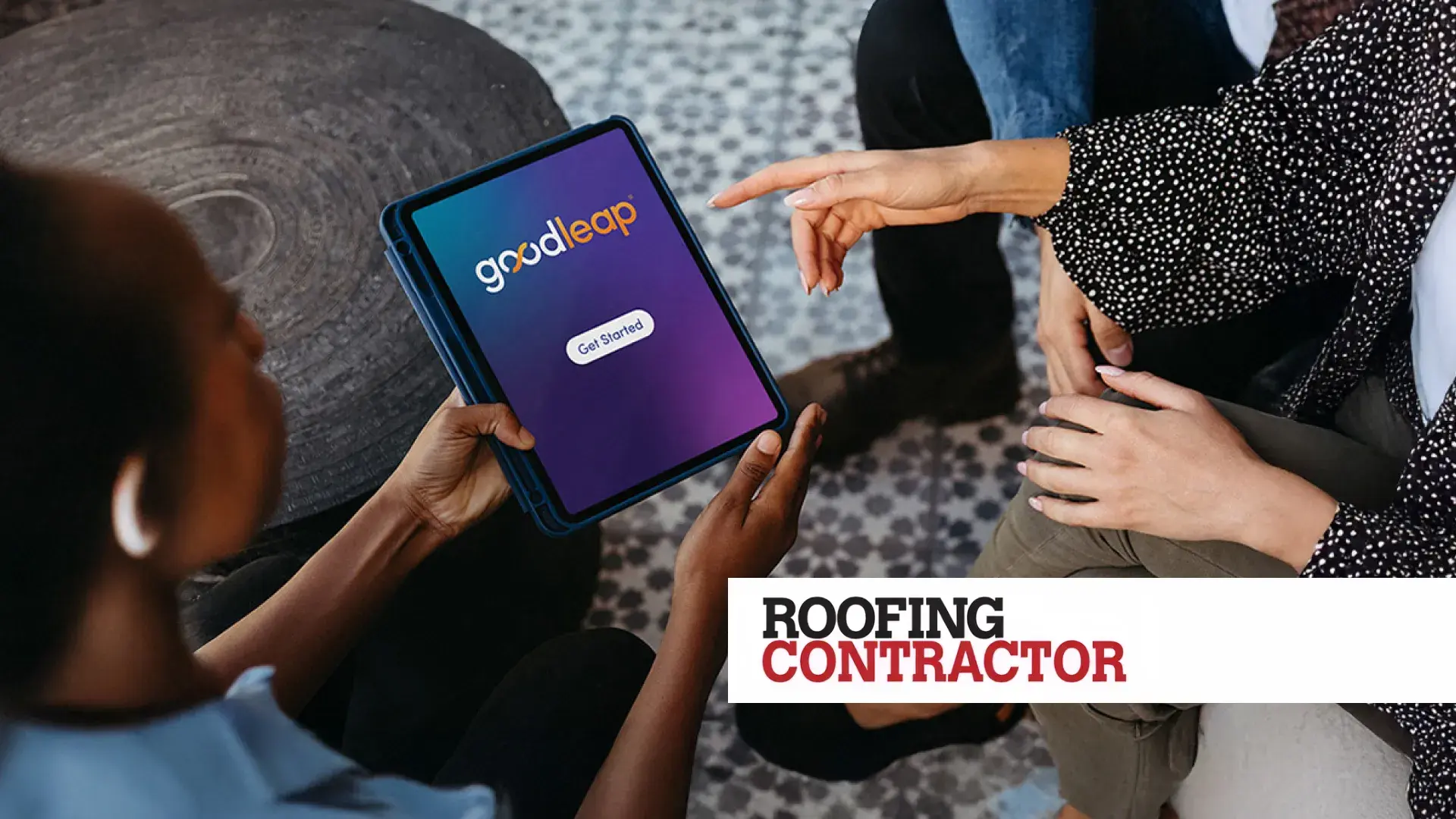 Two people sitting across from each other in conversation, with one person holding a tablet displaying the GoodLeap app interface. The screen shows a purple gradient background with the GoodLeap logo and a “Get Started” button. The person across is pointing at the tablet. A “Roofing Contractor” label appears prominently in the lower-right corner of the image.
