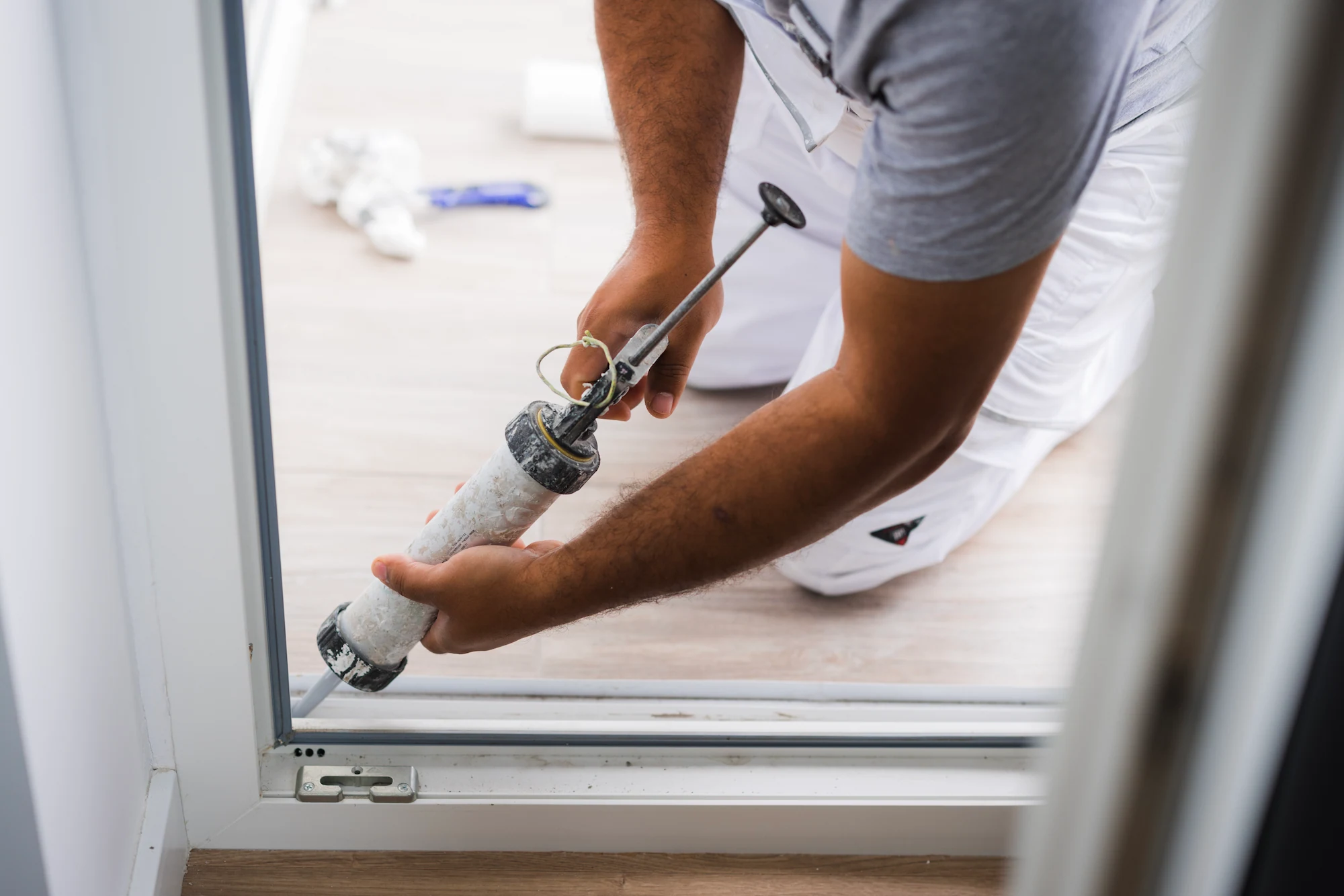 Person sealing the bottom edge of a sliding glass door with a caulking gun