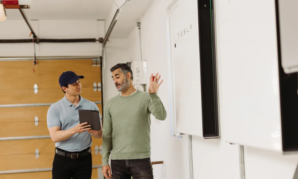 Sales professional talking with a homeowner in their garage with home batteries on the wall