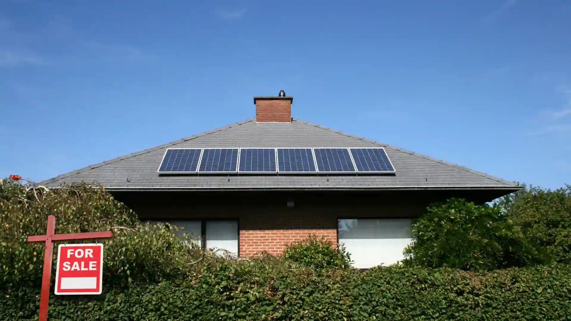 House with solar panels on roof and a For Sale sign in front
