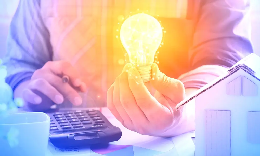 Person holding a light bulb and a calculator on a desk