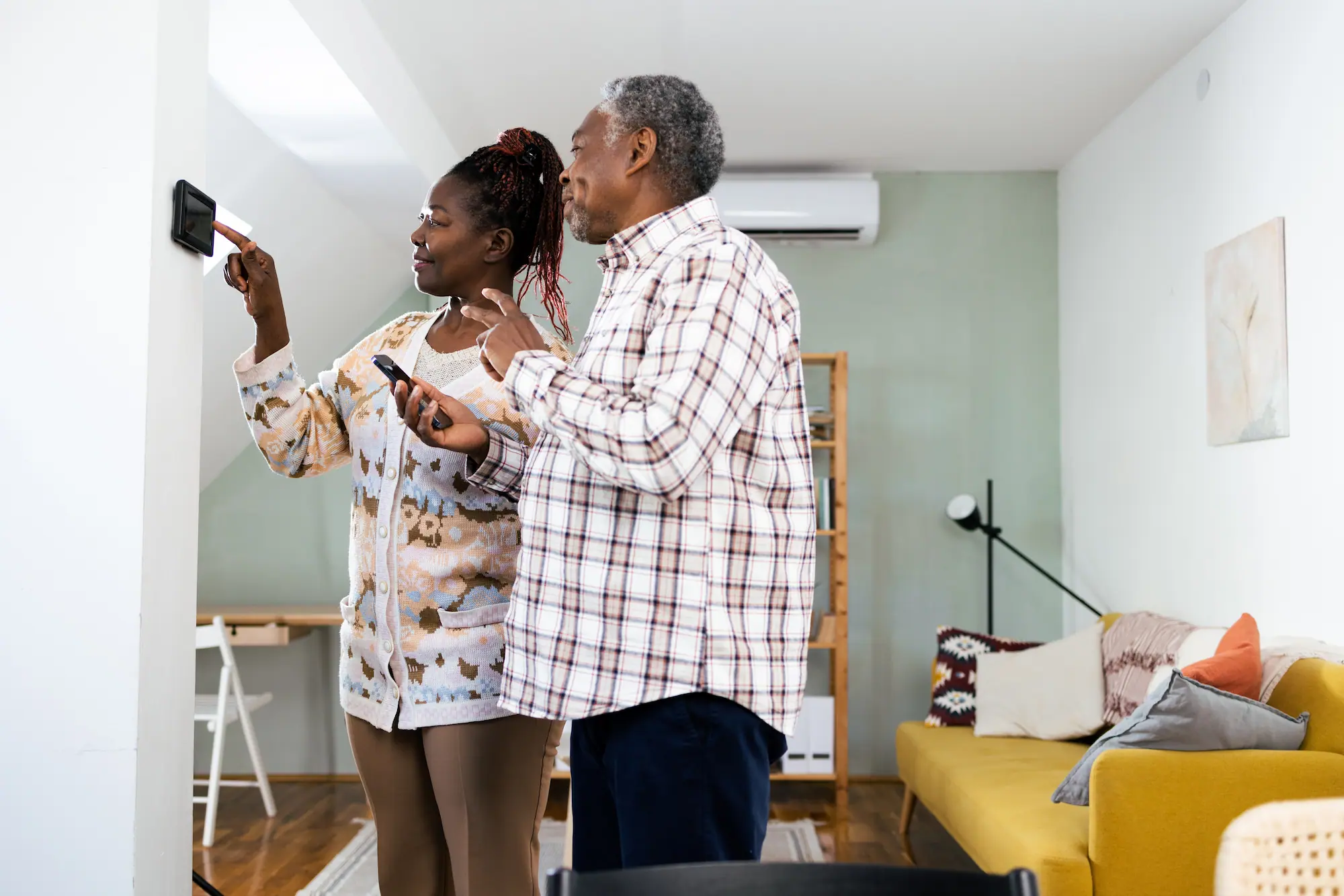 Smiling couple adjusting a smart thermostat on the wall in their modern living room