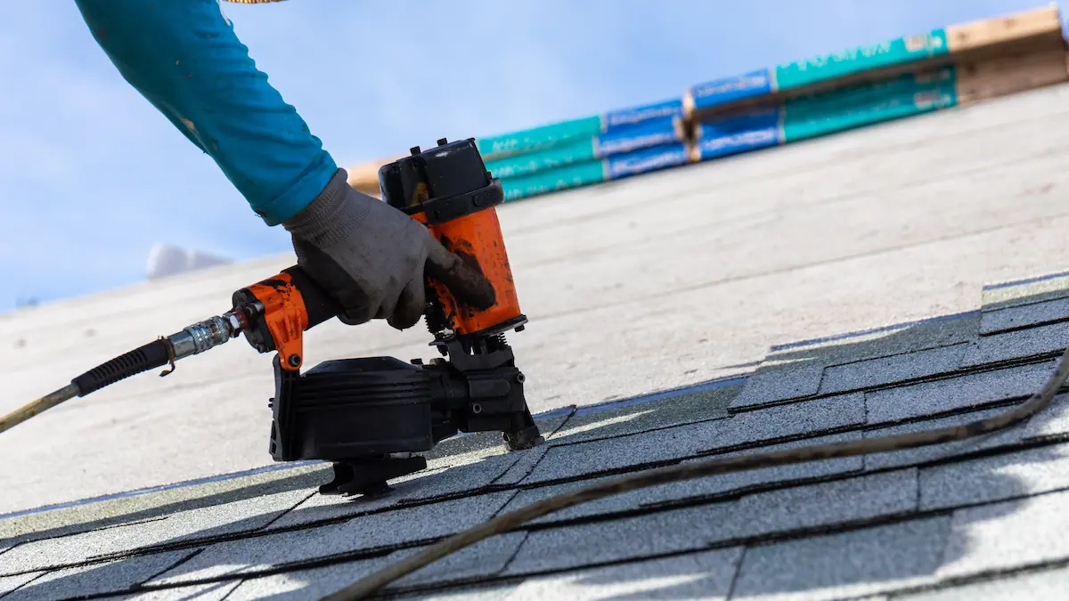 Installer nailing shingles to a roof